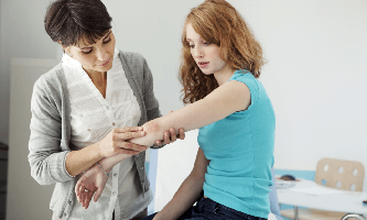 Una doctora pasa observa el codo de una paciente con psoriasis